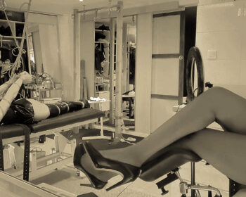 Jupe de cuir et talon hauts, Maîtresse Akina prend une pause en admirant sa dernière création, un beau strap-ado allongé